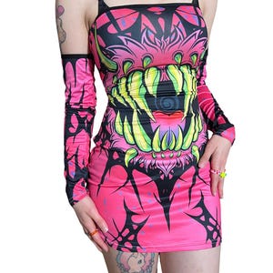 May include: A vibrant pink mini dress with a bold, monster-themed graphic. The design features a large, toothy mouth in shades of green and yellow, outlined in black. Includes matching long sleeves. The dress has a square neckline and thin straps.