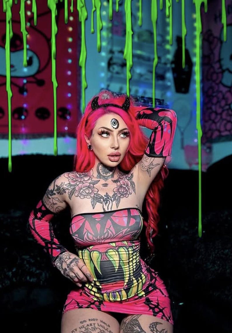 May include: A person with vibrant pink hair and elaborate tattoos, wearing a pink and black patterned tube top, matching gloves, and a mini skirt. Accessories include a horned headband and face jewelry. The background features neon green drips.