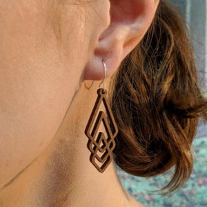 May include: A pair of wooden earrings with a geometric design. The earrings are brown and have a diamond shape. They are hanging from silver hooks.