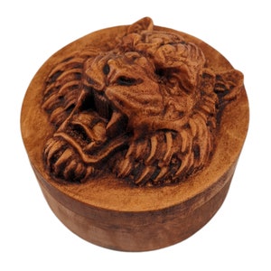 Round wooden box 3D carved with a tigers face looking straight ahead scowling and and showing its large fangs. It has burly fur on the sides of its face and chin. Made from hard maple wood stained brown against a white background.