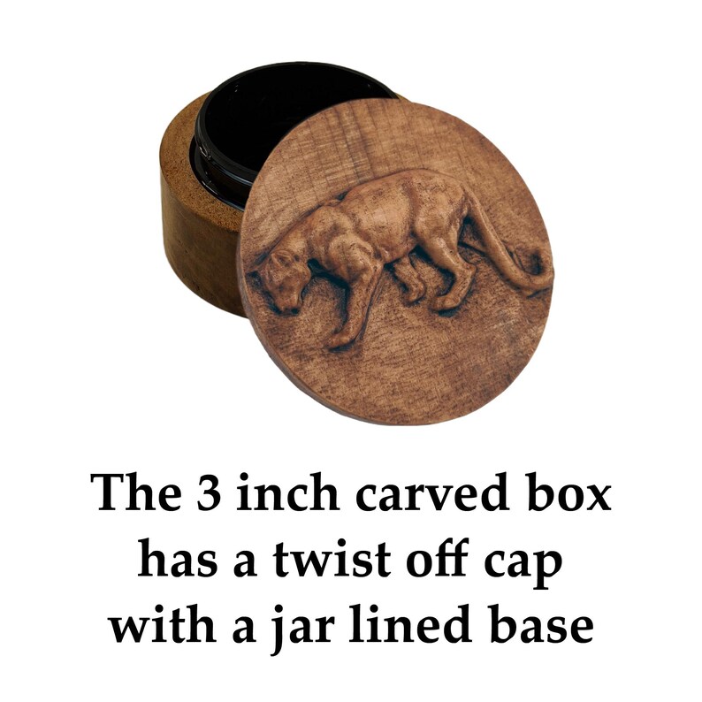May include: A 3 inch round wooden box with a twist-off cap featuring a carved panther design on the top surface. The container has a dark, smooth interior lining. The text below the object reads: The 3 inch carved box has a twist off cap with a jar lined base.