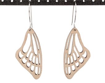 Puede incluir: Un par de pendientes de mariposa de madera con intrincados recortes. Los pendientes son de color marrón claro y tienen ganchos plateados.