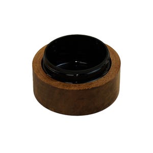 May include: A small, cylindrical container featuring a natural brown wooden exterior and a smooth, glossy black interior. The vessel has a wide, open top with a circular rim, showcasing a distinct contrast between the organic wood grain and the dark, reflective inner surface of the bowl-like object.