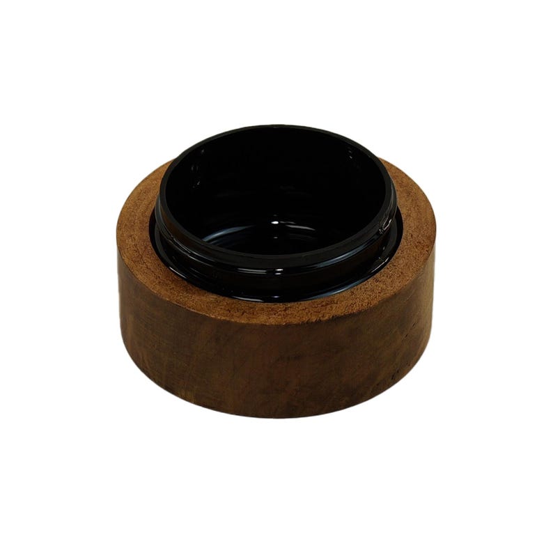 May include: A small, cylindrical container featuring a natural brown wooden exterior and a smooth, glossy black interior. The vessel has a wide, open top with a circular rim, showcasing a distinct contrast between the organic wood grain and the dark, reflective inner surface of the bowl-like object.