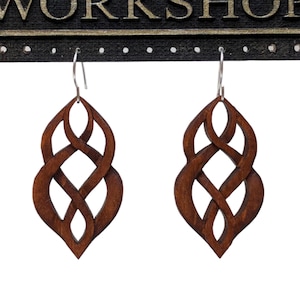 Könnte beinhalten: Ein Paar braune Holzohrringe mit einem keltischen Knotendesign. Die Ohrringe hängen an silbernen Haken.