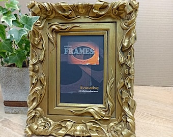 May include: A gold picture frame with ornate details and a black mat. The frame has a label that reads "picture FRAMES Evocative alexlutsenko.net".