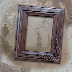 Può includere: Una cornice per foto in legno marrone scuro con un design intagliato nell'angolo in basso a destra. La cornice è vuota e ha una leggera lucentezza.