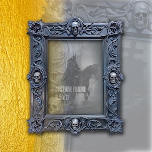 May include: Ornate black picture frame with skull accents. The frame is rectangular with intricate floral and skull carvings. The text "PICTURE FRAME 8.5 x 11" is visible. The frame is designed to hold an 8.5 x 11 inch picture.