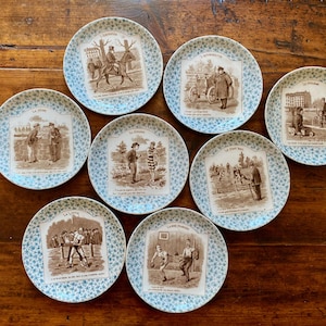 Set di piatti antichi francesi in maiolica di Digoin Sarreguemines: scene sportive, decorazione a decalcomania seppia, bordo blu-verde.