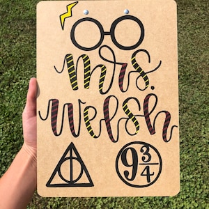 May include: A brown clipboard with a Harry Potter theme. It has a lightning bolt, glasses, the words "Mrs. Welsh", the Deathly Hallows symbol, and the number "9 3/4" in a circle.