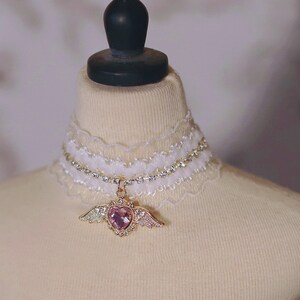 May include: A white lace choker with a rhinestone chain and a pink heart charm with gold wings.