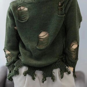 May include: A dark green sweater with distressed detailing and frayed edges. The sweater has several large holes throughout.