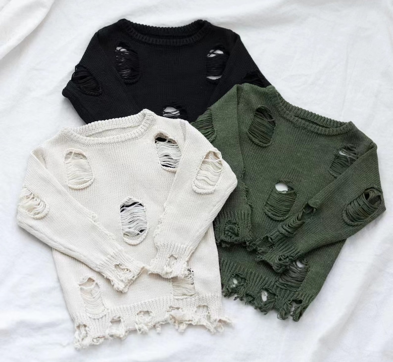 May include: Three distressed knit jumpers in black, white and green. The jumpers have a round neckline and long sleeves. The jumpers are made of a soft, comfortable material and have a distressed look with holes and frayed edges.