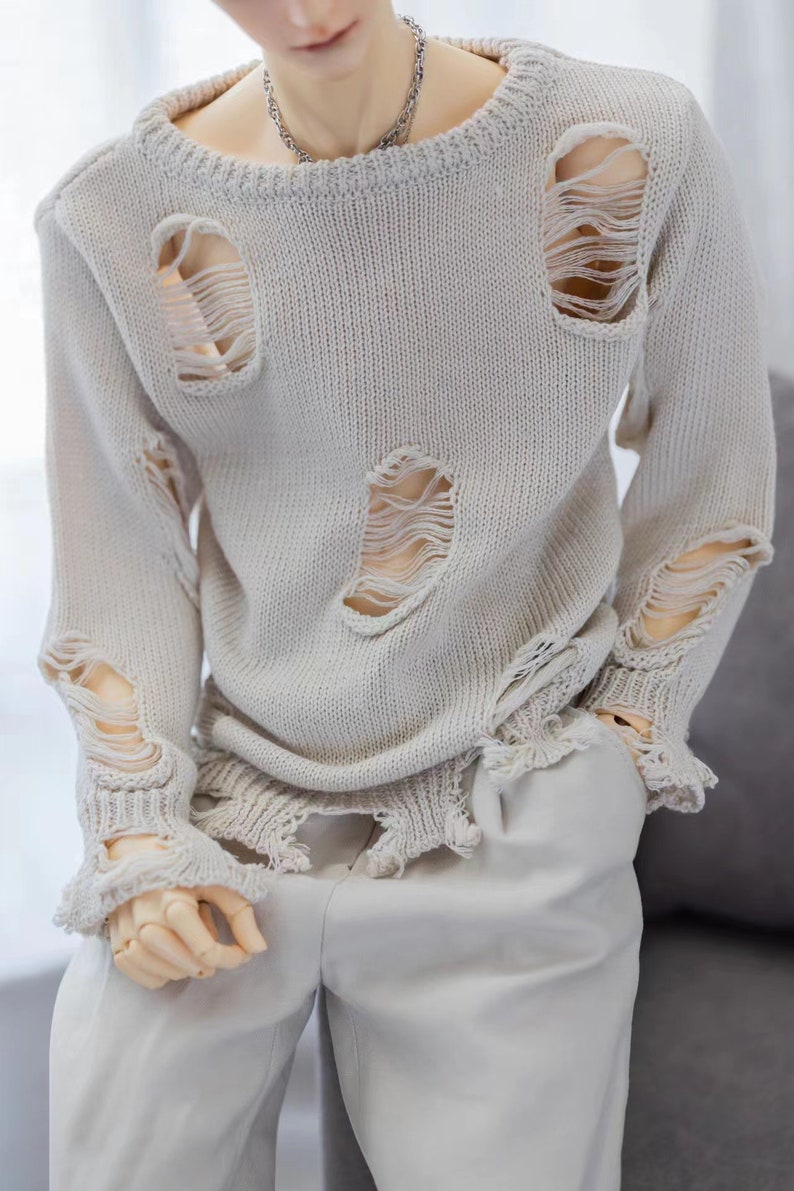 May include: A light beige sweater with distressed detailing and frayed edges. The sweater has several large holes throughout.