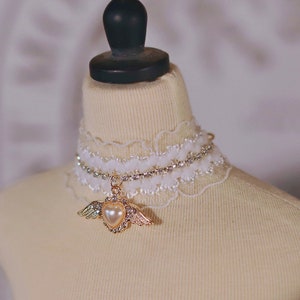 May include: A white lace choker with a rhinestone chain and a gold heart pendant with pearl accents and wings.