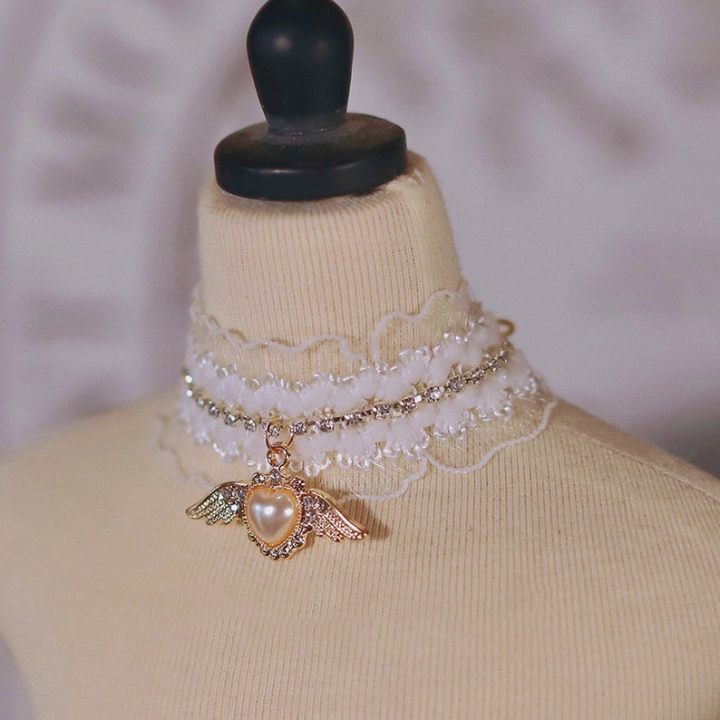 May include: A white lace choker with a rhinestone chain and a gold heart pendant with pearl accents and wings.