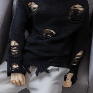 May include: A black distressed knit sweater with a crew neck and long sleeves. The sweater has several large holes and frayed edges.