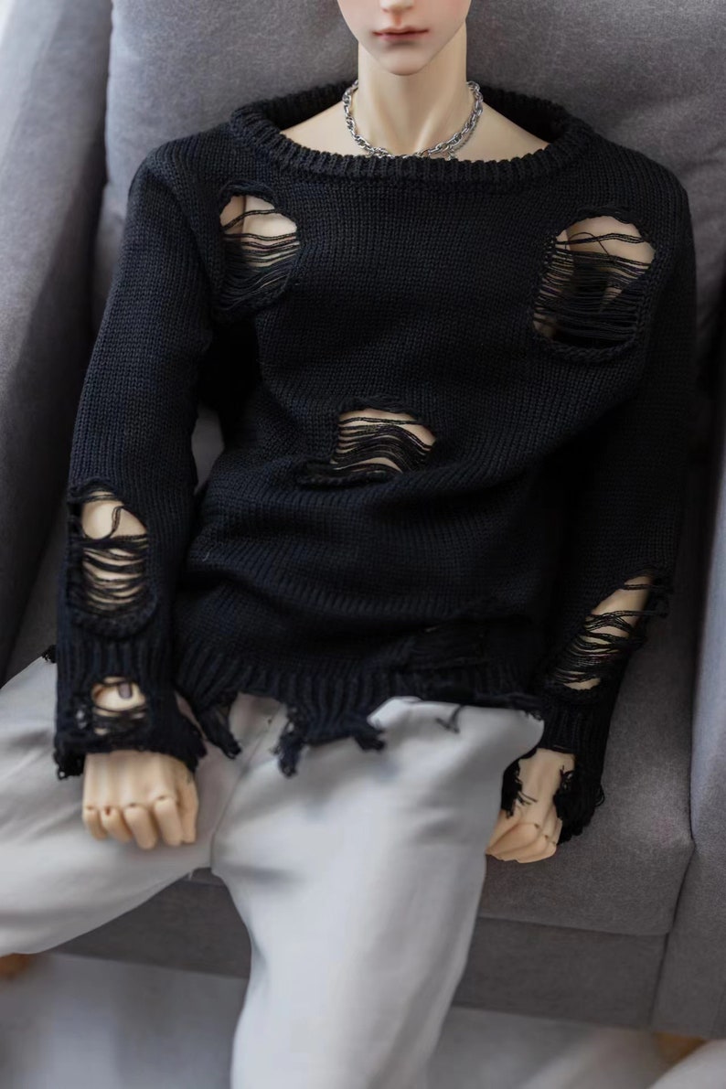 May include: A black distressed knit sweater with a crew neck and long sleeves. The sweater has several large holes and frayed edges.