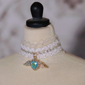 May include: White lace choker with a rhinestone chain and a gold pendant featuring a blue heart with wings.