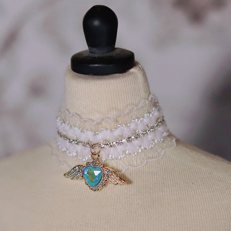 May include: White lace choker with a rhinestone chain and a gold pendant featuring a blue heart with wings.