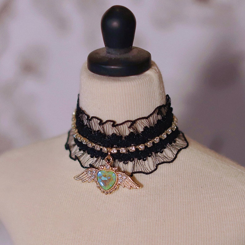 May include: A black lace choker with a rhinestone trim and a gold heart pendant with iridescent green wings.