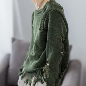 May include: A green distressed sweater with frayed edges and holes throughout. The sweater has a crew neck and long sleeves.