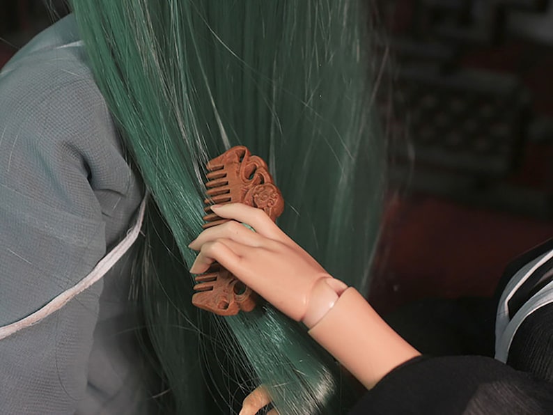 Puede incluir: Una mano sosteniendo un peine de madera con tallas intrincadas. El peine se est&aacute; utilizando para cepillar el cabello largo y verde.