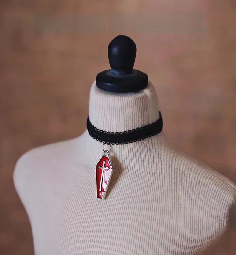 May include: A black choker necklace with a silver pendant shaped like a red coffin with a white cross on it.