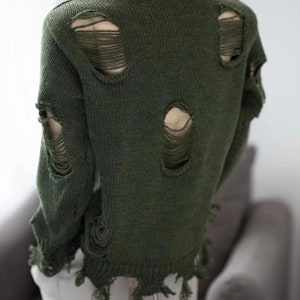 May include: A dark green knitted jumper with distressed detailing and holes throughout. The jumper has a relaxed fit and a slightly cropped length.