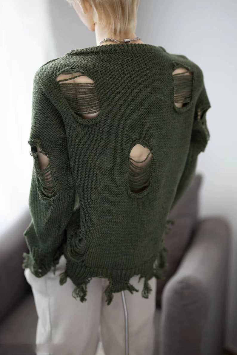 May include: A dark green knitted jumper with distressed detailing and holes throughout. The jumper has a relaxed fit and a slightly cropped length.