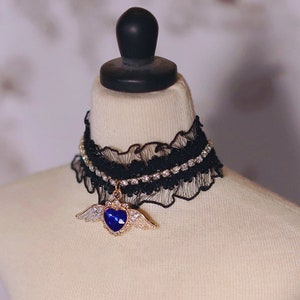 May include: A black lace choker with a rhinestone trim and a gold pendant featuring a blue heart with wings.