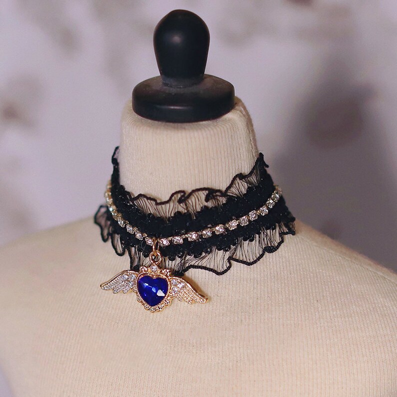May include: A black lace choker with a rhinestone trim and a gold pendant featuring a blue heart with wings.
