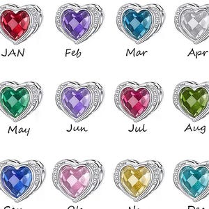 May include: A collection of heart-shaped charms, each with a different colored gemstone and a silver-colored border. Each charm has a month of the year labeled on it: Jan, Feb, Mar, Apr, May, Jun, Jul, Aug, Sep, Oct, Nov, and Dec.