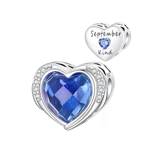 May include: A silver heart-shaped charm with a large, faceted blue gemstone center, surrounded by small clear crystals. A smaller heart charm with the words "September Kind" and a blue gemstone is also shown.