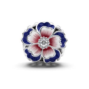 May include: A silver-toned floral charm with a central cluster of clear stones. The flower features white, pink, and dark blue enamel petals. The charm is round and has a detailed design.