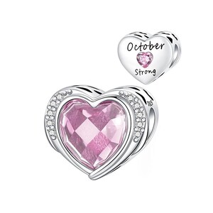 May include: A silver heart-shaped charm with a large pink gemstone center, surrounded by small clear crystals. A smaller heart charm with the words "October Strong" and a pink gemstone is also visible.