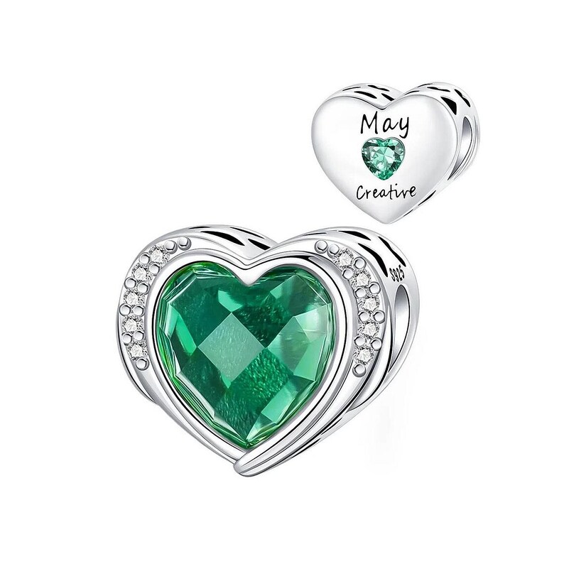 May include: A silver heart-shaped charm with a large, faceted green gemstone center, surrounded by small clear crystals. A smaller heart charm with the word "May" and "Creative" and a green gemstone is also shown.