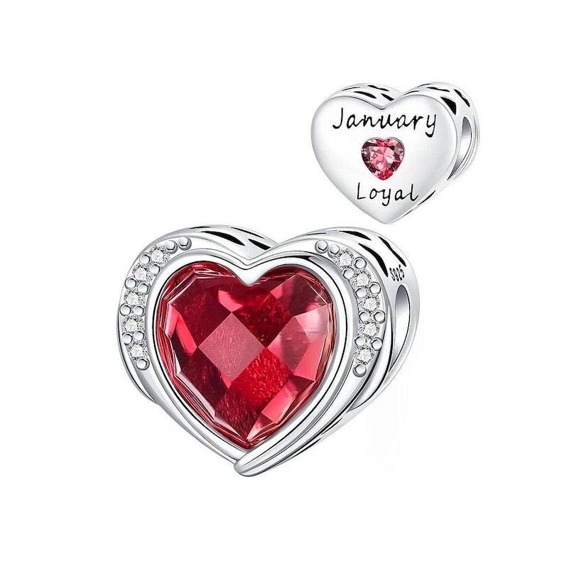 May include: A silver heart-shaped charm with a large, faceted red gemstone center, surrounded by a row of small clear crystals. A smaller heart charm with the words "January" and "Loyal" and a pink gemstone is also shown.