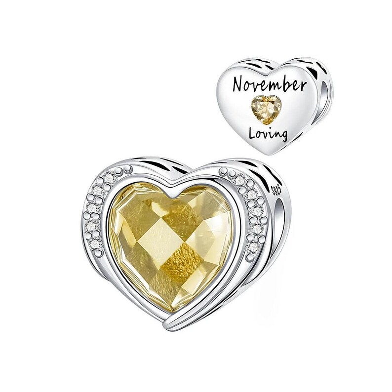 May include: A silver heart-shaped charm with a large, faceted yellow gemstone center. The charm is accented with small clear crystals around the edge. A smaller heart charm with the words "November Loving" and a yellow gemstone is also present.