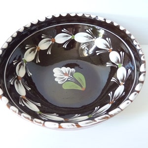 以下が含まれることがあります： 白と緑の花柄が描かれた茶色の陶器のボウル。ボウルは波打った縁と光沢のある仕上げになっています。