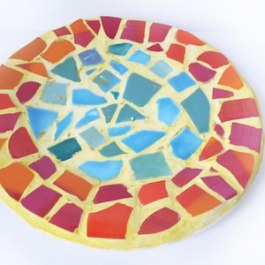 Könnte beinhalten: Eine runde, gelbe Keramikschale mit einem Mosaikdesign. Das Mosaik besteht aus kleinen, bunten Fliesen in Rot-, Orange-, Blau- und Grüntönen.