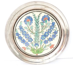 Op de afbeelding: Een rond keramisch bord met een zilveren rand heeft een bloemenmotief met blauwe, groene en rode bloemen. Het bord is perfect om snacks of desserts op te serveren.