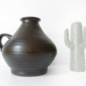 Può includere: Un vaso in ceramica marrone con manico e una scultura di cactus in ceramica bianca.