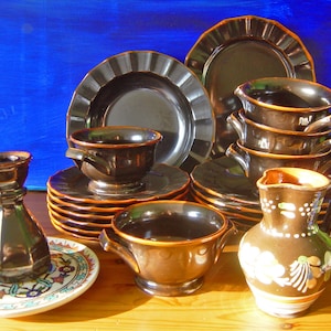 Può includere: Un set di piatti e ciotole in ceramica marrone con finiture dorate. Il set comprende una brocca, un portacandele e diversi piatti e ciotole.