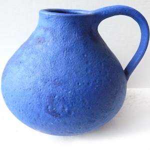 Può includere: Un'anfora in ceramica blu con una superficie testurizzata e un corpo arrotondato. L'anfora ha un manico e un'ampia apertura.
