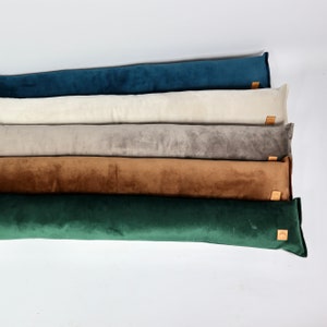 Peut inclure: Cinq longs coussins rectangulaires de différentes couleurs. Les coussins sont empilés les uns sur les autres. Les couleurs sont turquoise, crème, gris, marron et vert.