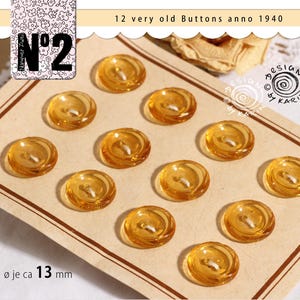 May include: Twelve vintage amber-colored buttons, each with a diameter of approximately 0.5 inches, arranged on a tan card. The buttons have a spiral design and a white thread. The card has text that reads "12 very old Buttons anno 1940".