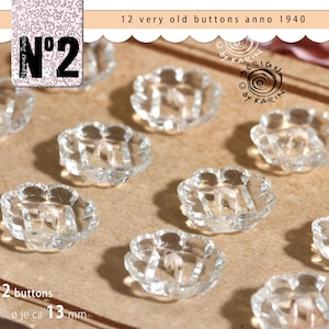 Puede incluir: Doce botones antiguos de vidrio transparente con diseño floral. Cada botón, de 1940, mide aproximadamente 1,3 cm de diámetro. Se muestran sobre una superficie marrón claro. El texto "N°2" y "12 very old buttons anno 1940" es visible.