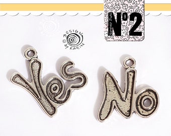 Könnte beinhalten: Zwei silberne Anhänger, einer mit dem Wort "Ja" und der andere mit dem Wort "Nein". Beide Anhänger haben oben ein Loch zum Anbringen an einer Kette oder einem Armband.