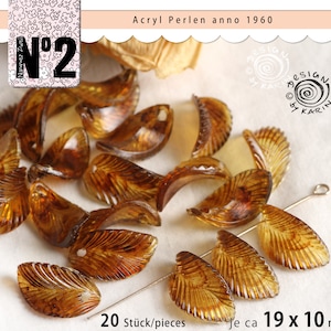 Può includere: Una collezione di 20 perline in acrilico a forma di foglia di colore ambrato, ciascuna con un foro per l'infilaggio. Le perline misurano circa 19 mm per 10 mm. Le perline sono sparse su una superficie bianca. Il testo "N°2 Acryl Perlen anno 1960" è visibile nell'angolo in alto a sinistra dell'immagine.
